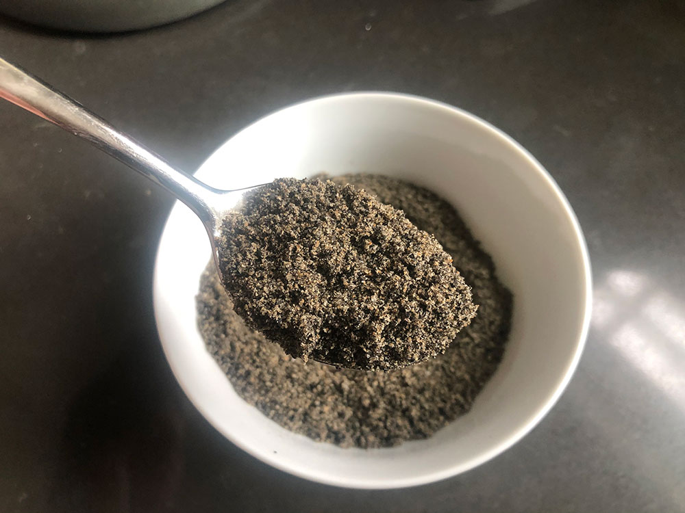 spoonful of ground black sesame seeds with a white bowl in the background